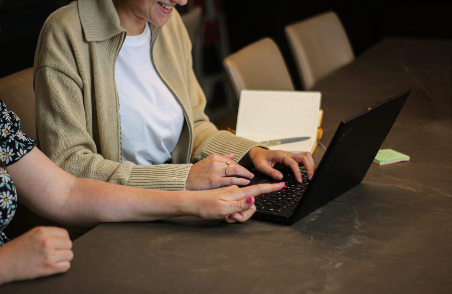 Up close of one hand pointing at a laptop screen that someone else is using